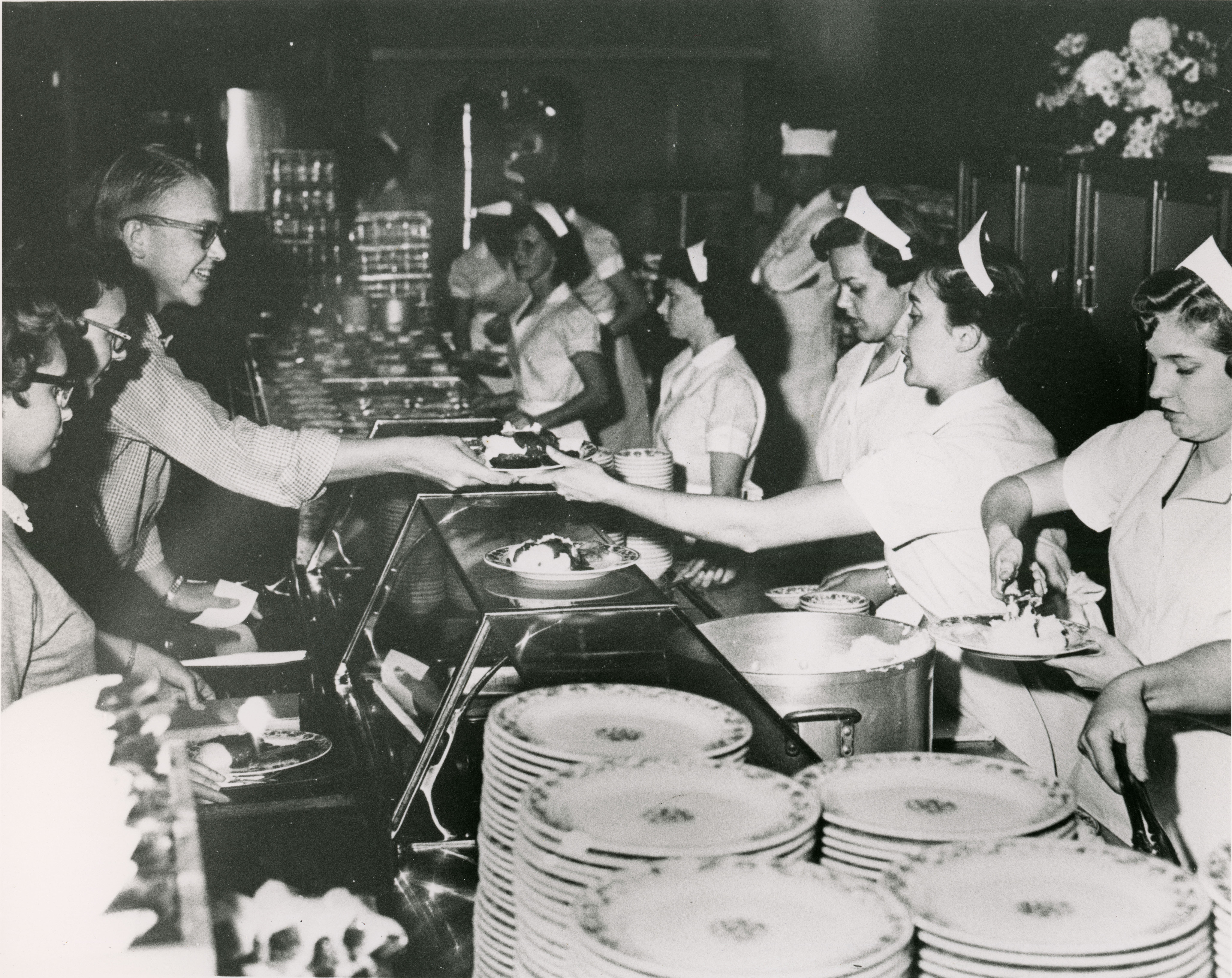 Women in uniforms loading food onto plates for students in cafeteria serving line