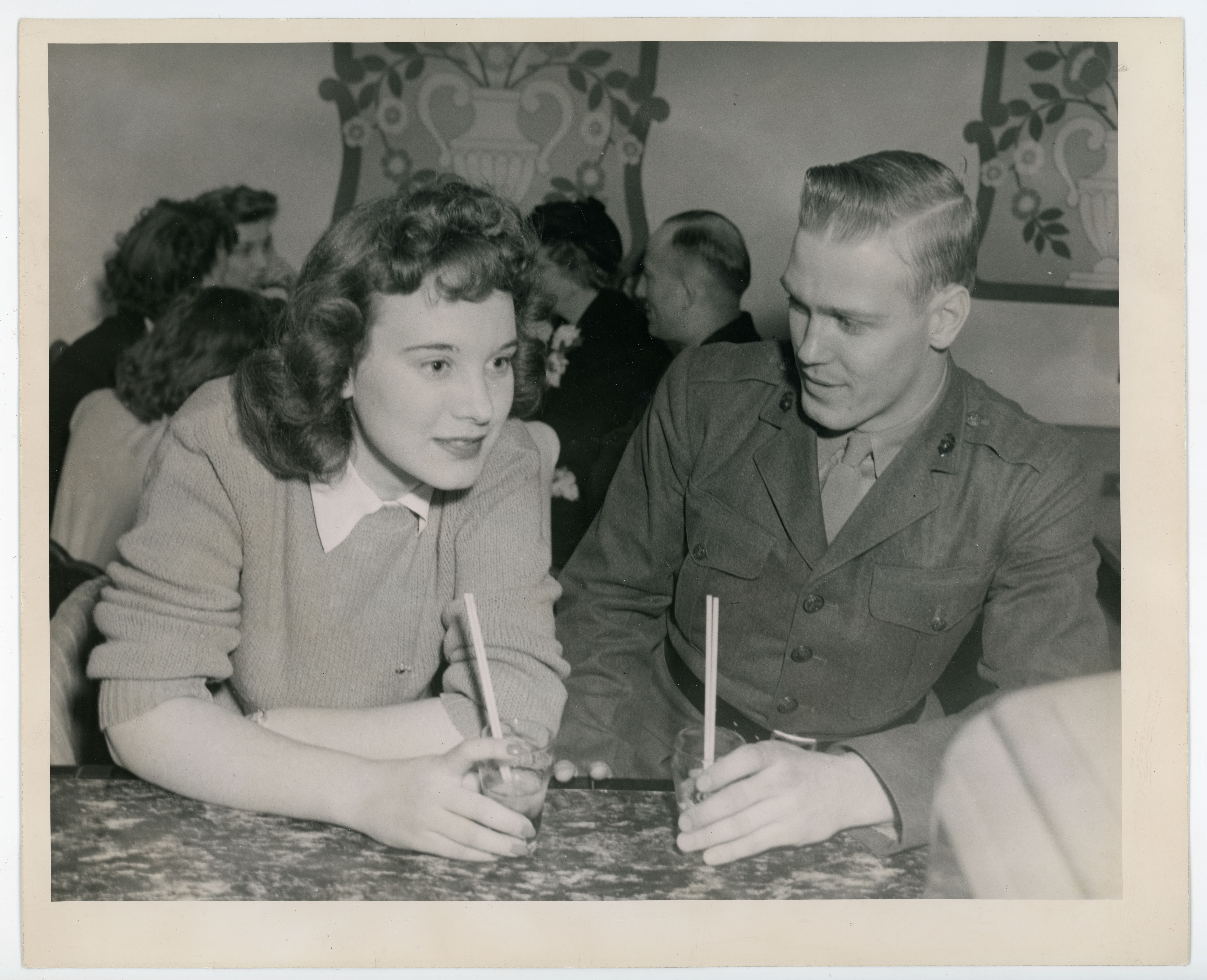 A woman and man conversing at a soda fountain counter, another group of people in the background