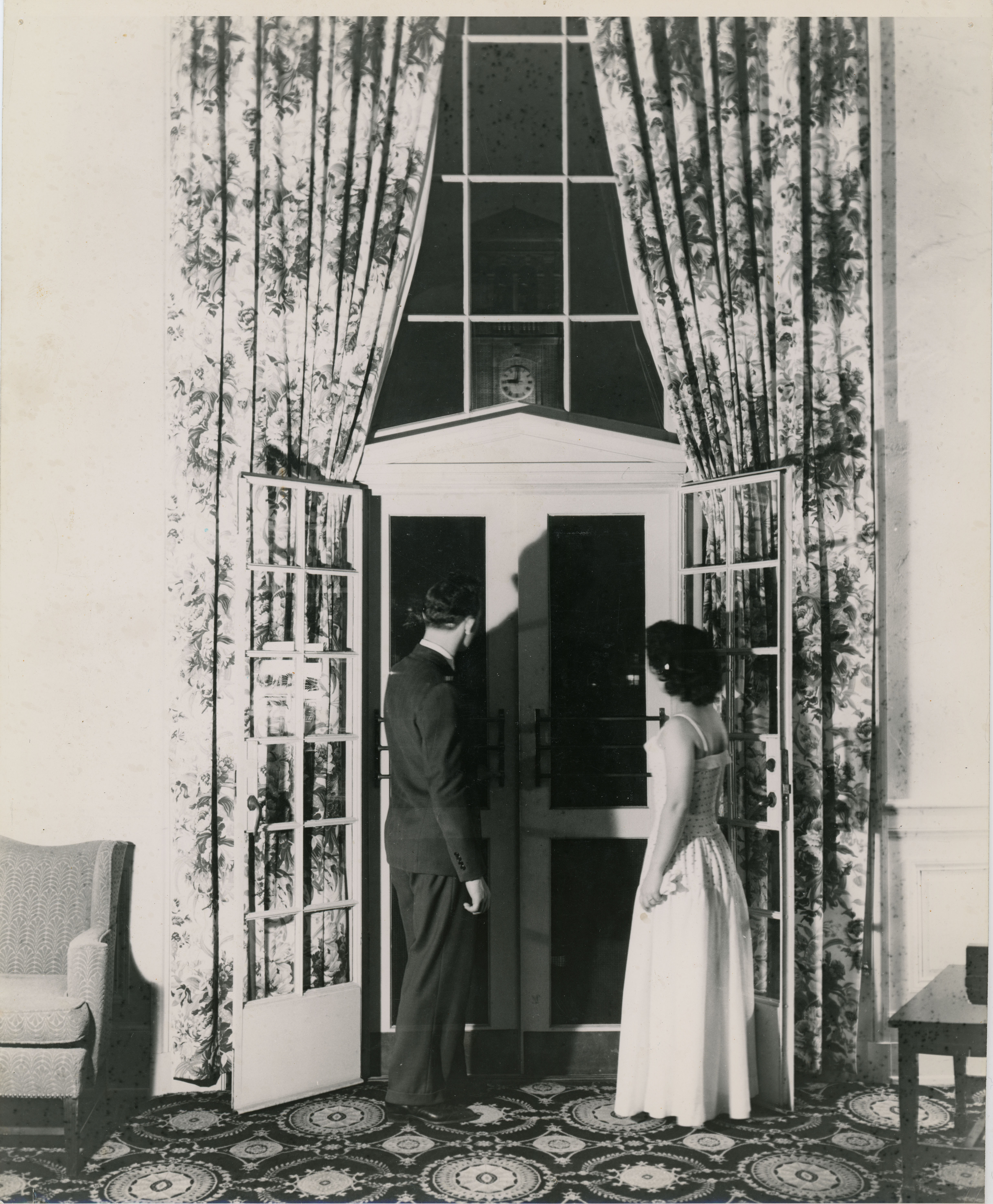 A man and woman in formal wear looking out a glass door at the Campanile