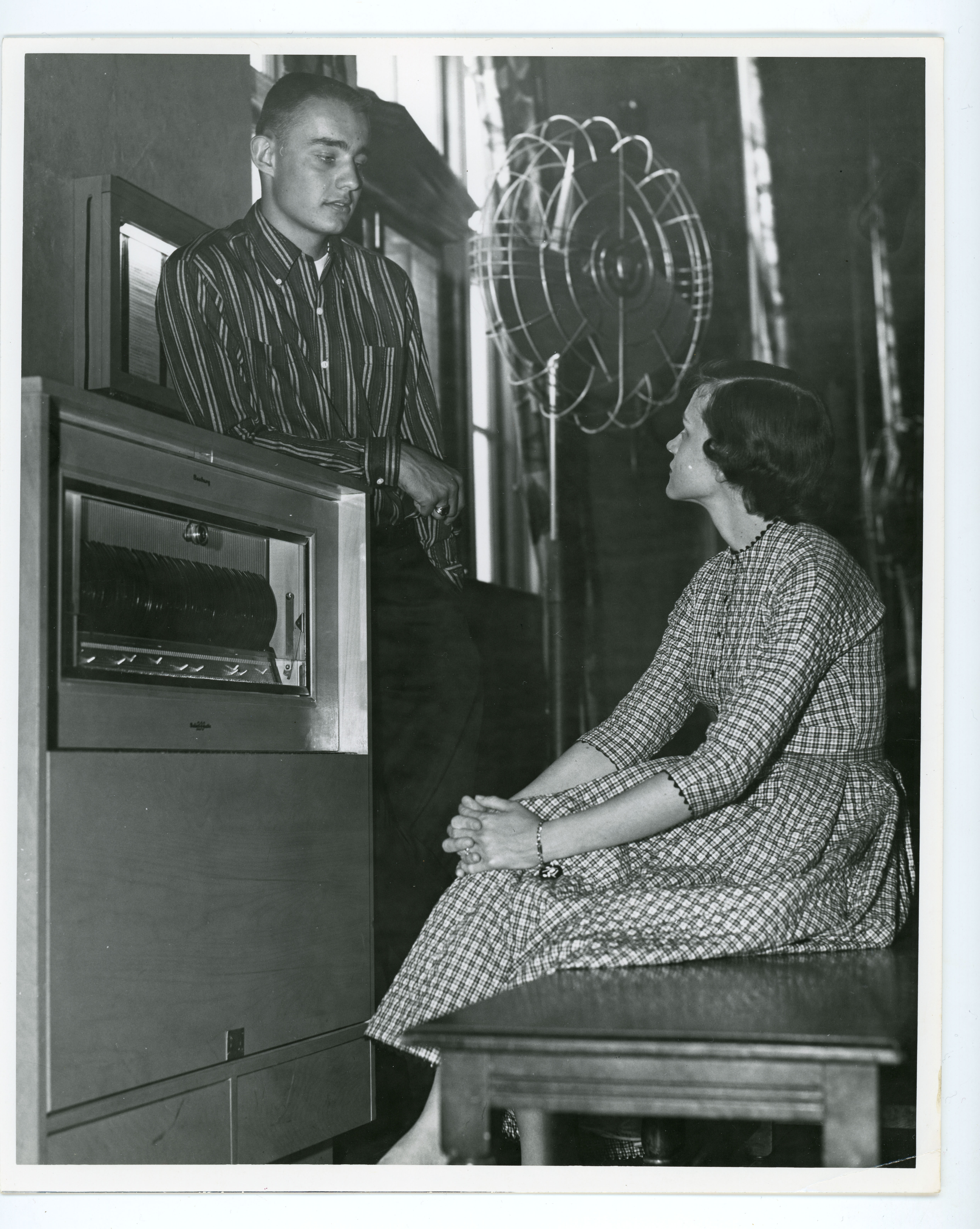 Man leaning on and woman seated on bench in front of a jukebox