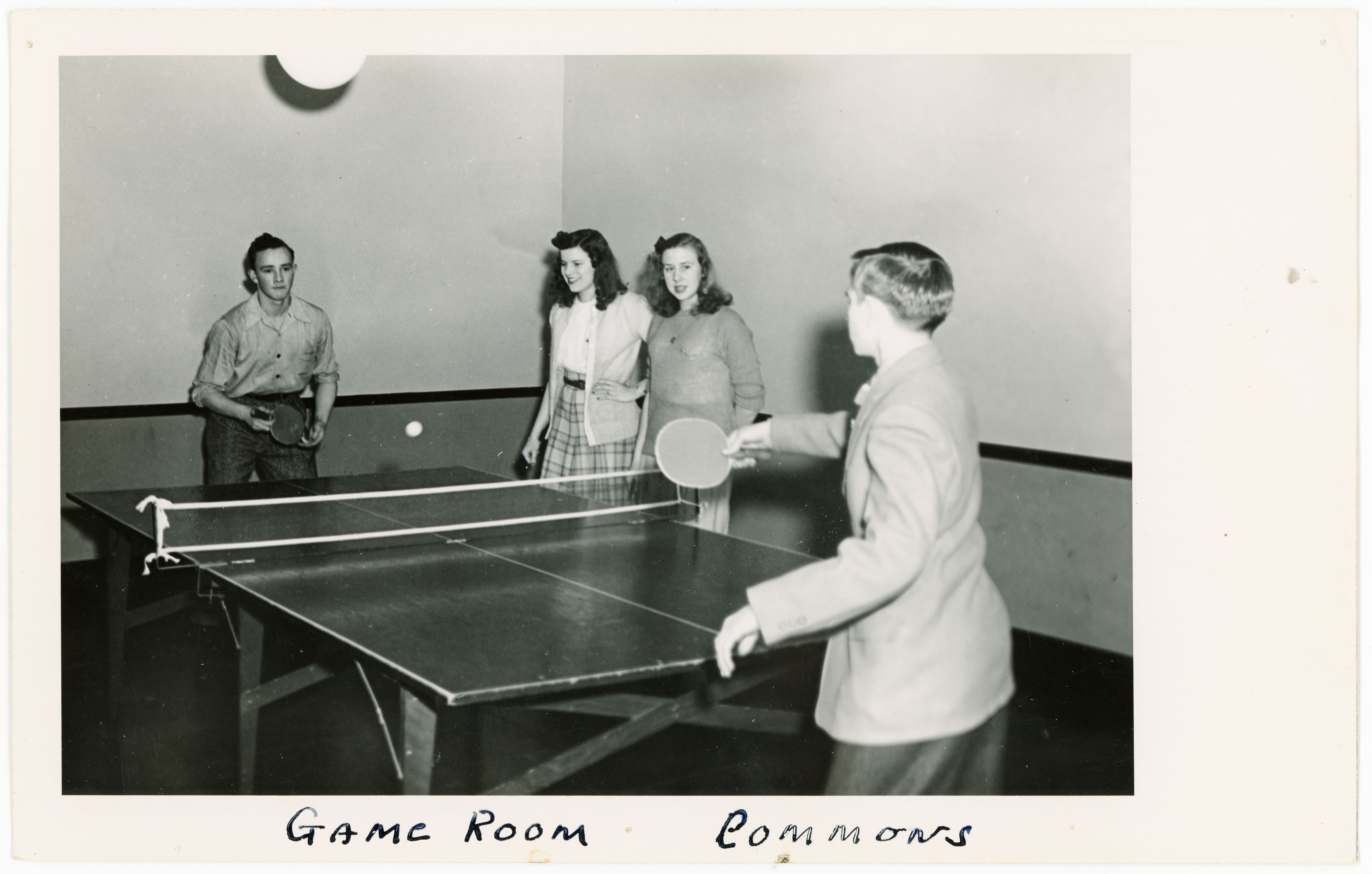 Two men playing ping pong and two women watching; handwritten caption reads Game Room Commons