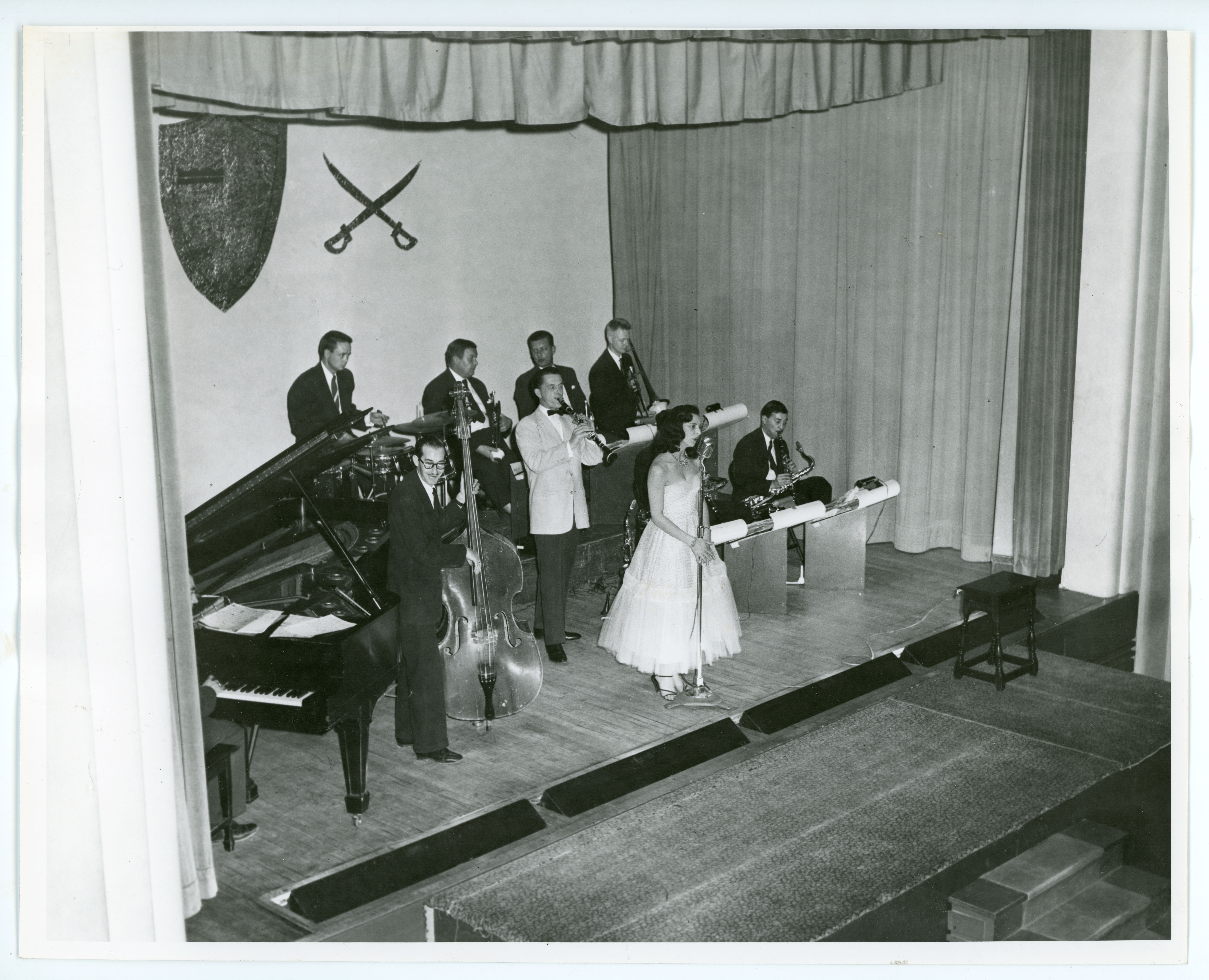 A woman singing on a stage with a band of seven men playing instruments