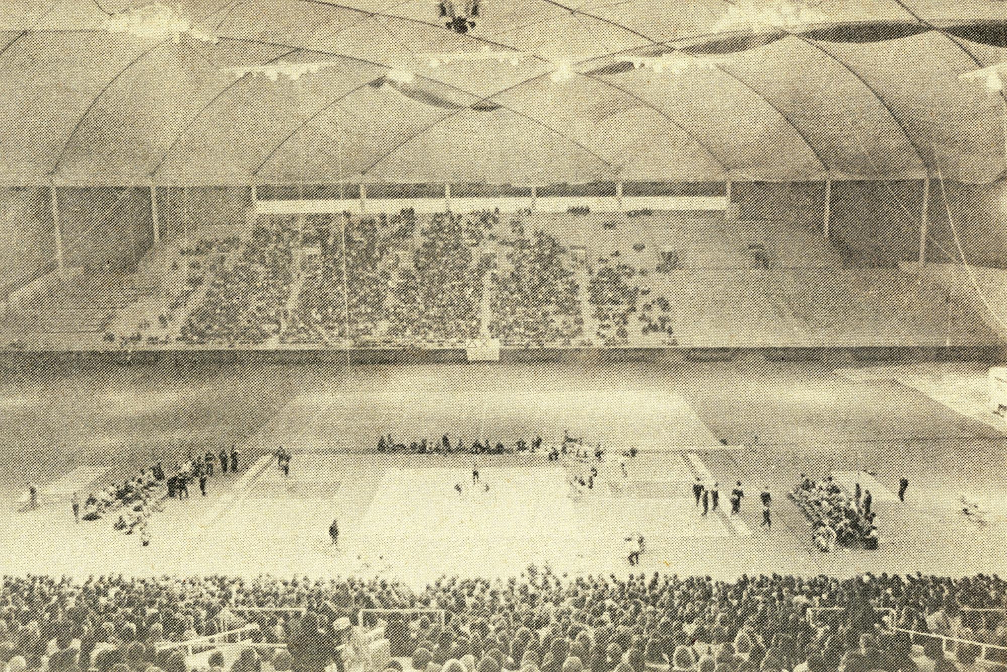 Taken from upper level looking down to floor, a wrestling meet with crowd filling seats on either side of field