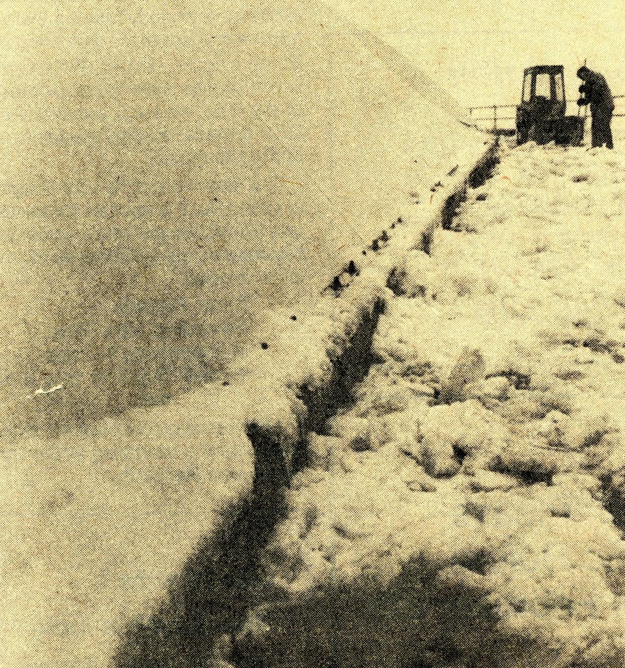 Outside where fabric of roof meets walkway, a person clearing snow from around the rim