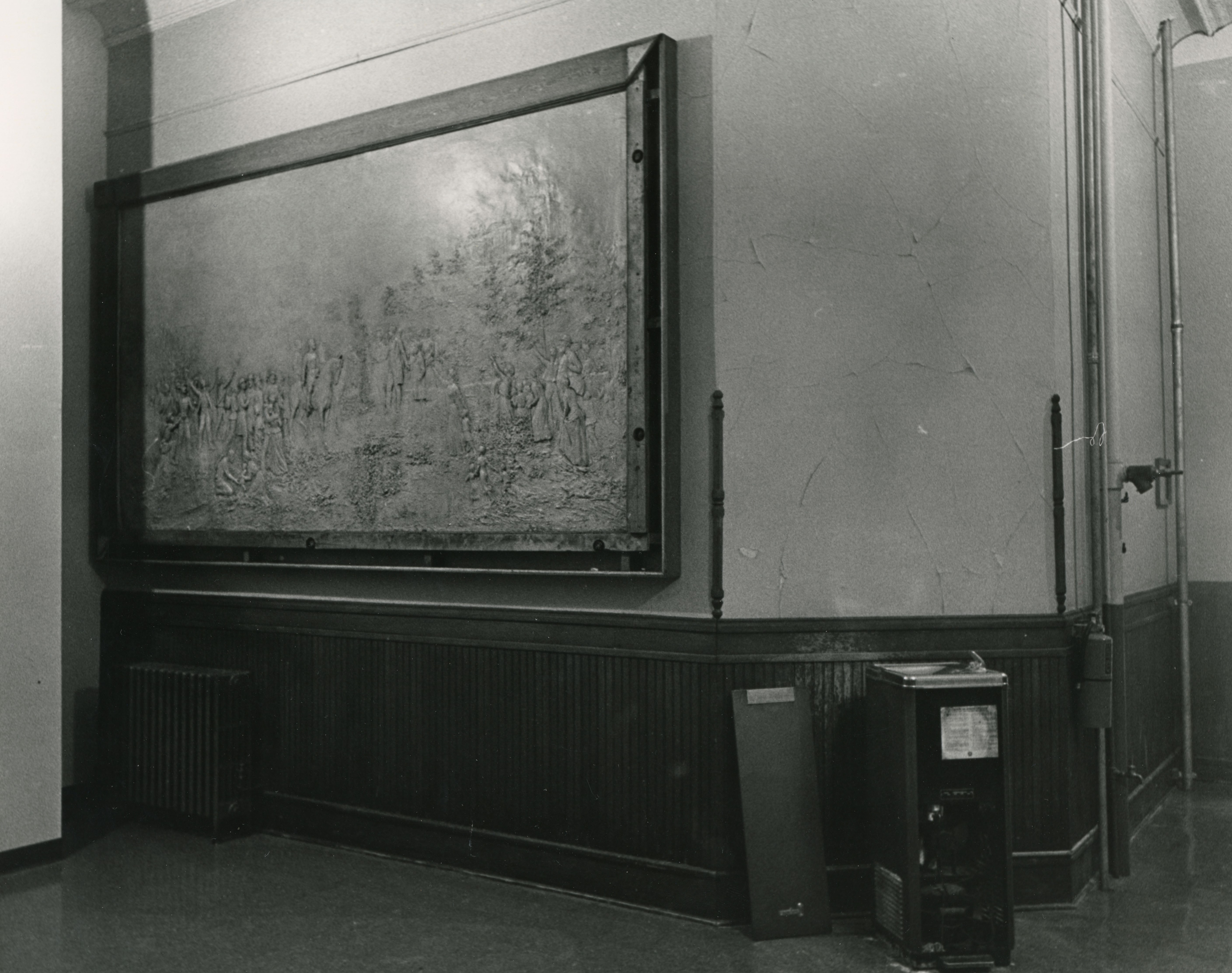 Framed metal cast of a battle scene and woman with children, mounted in a building's hallway