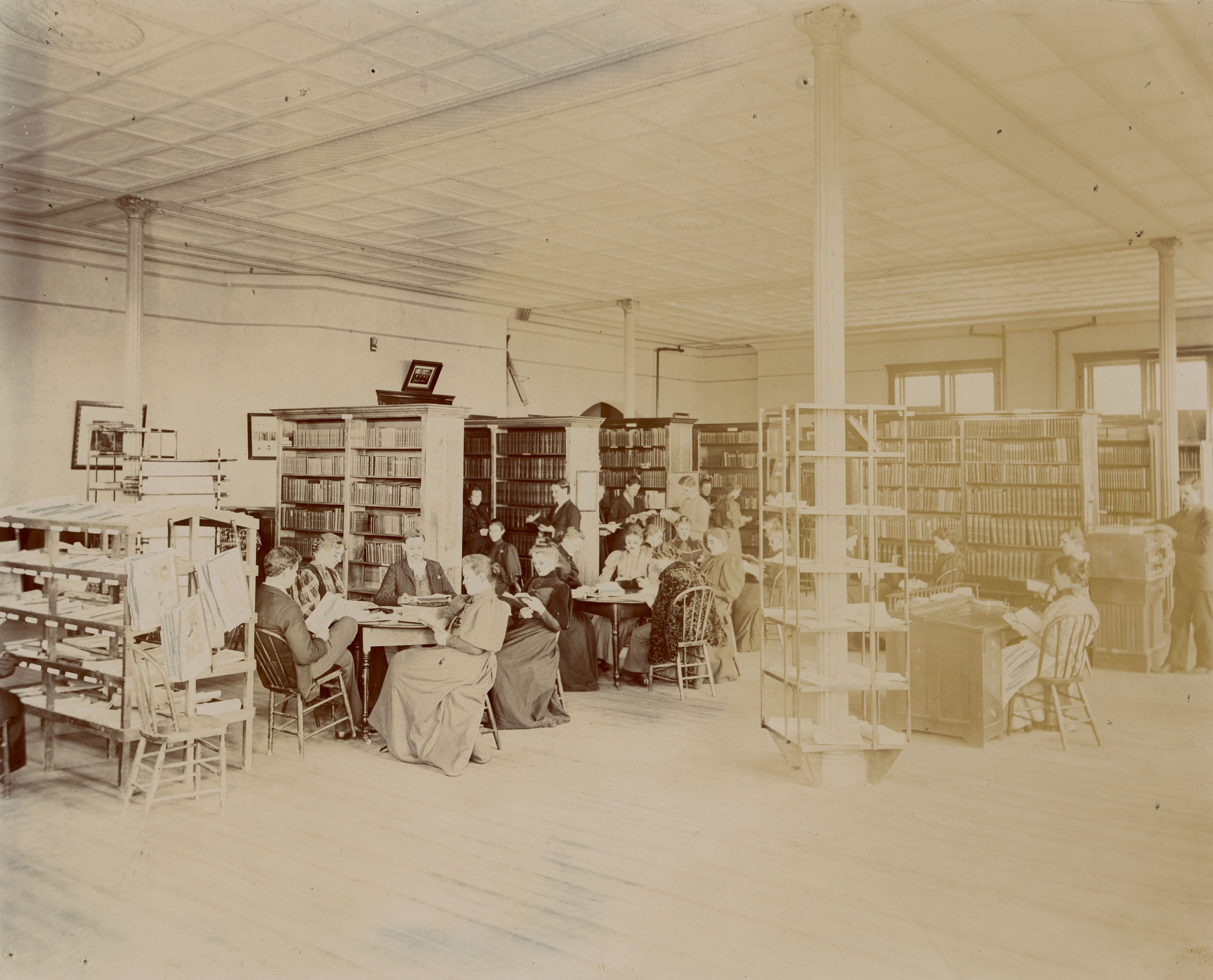Women and men studying, both standing and seated, in a room with library stacks