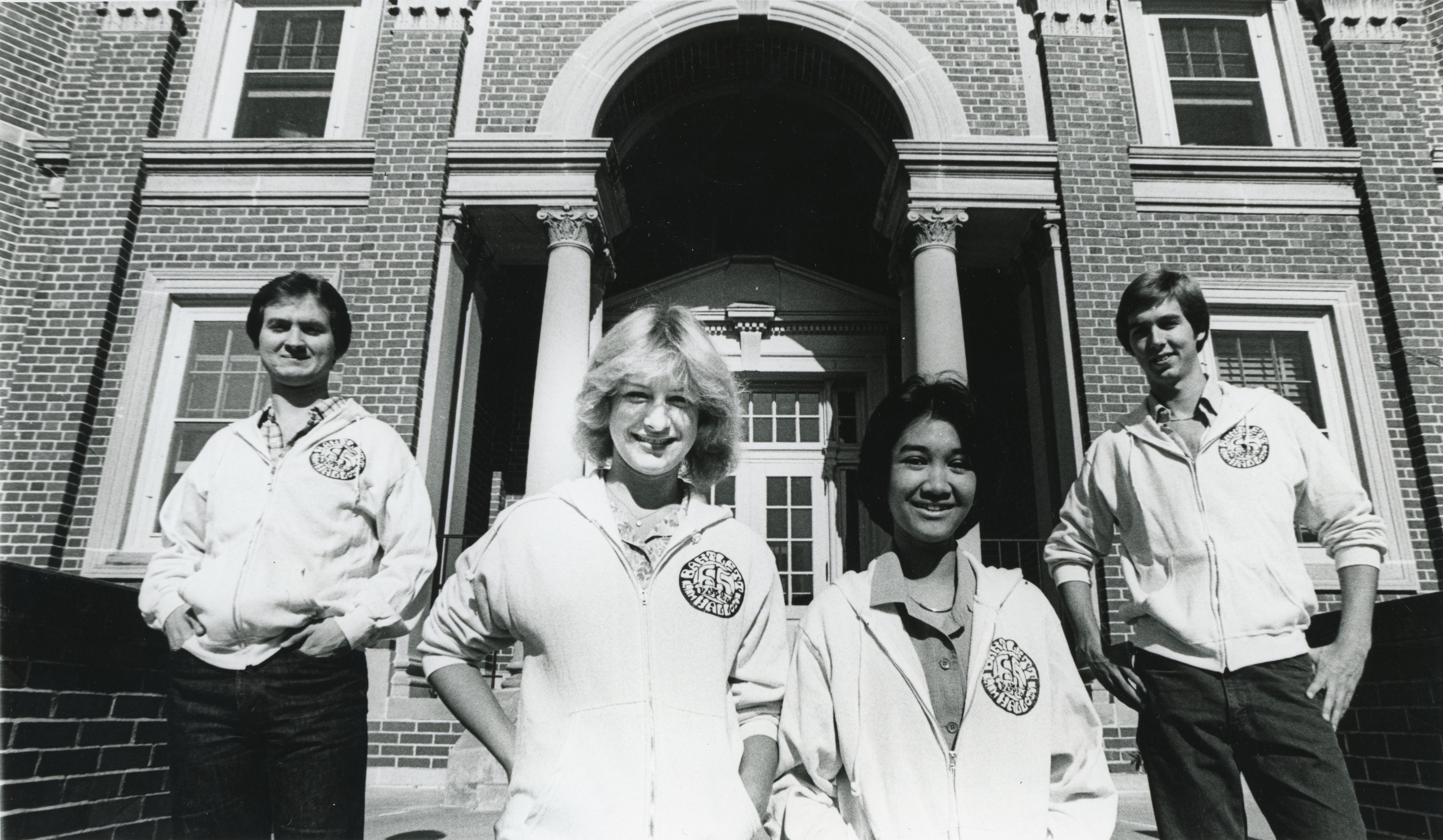Four people in matching sweatshirts posed on the steps at the entrance to a brick building