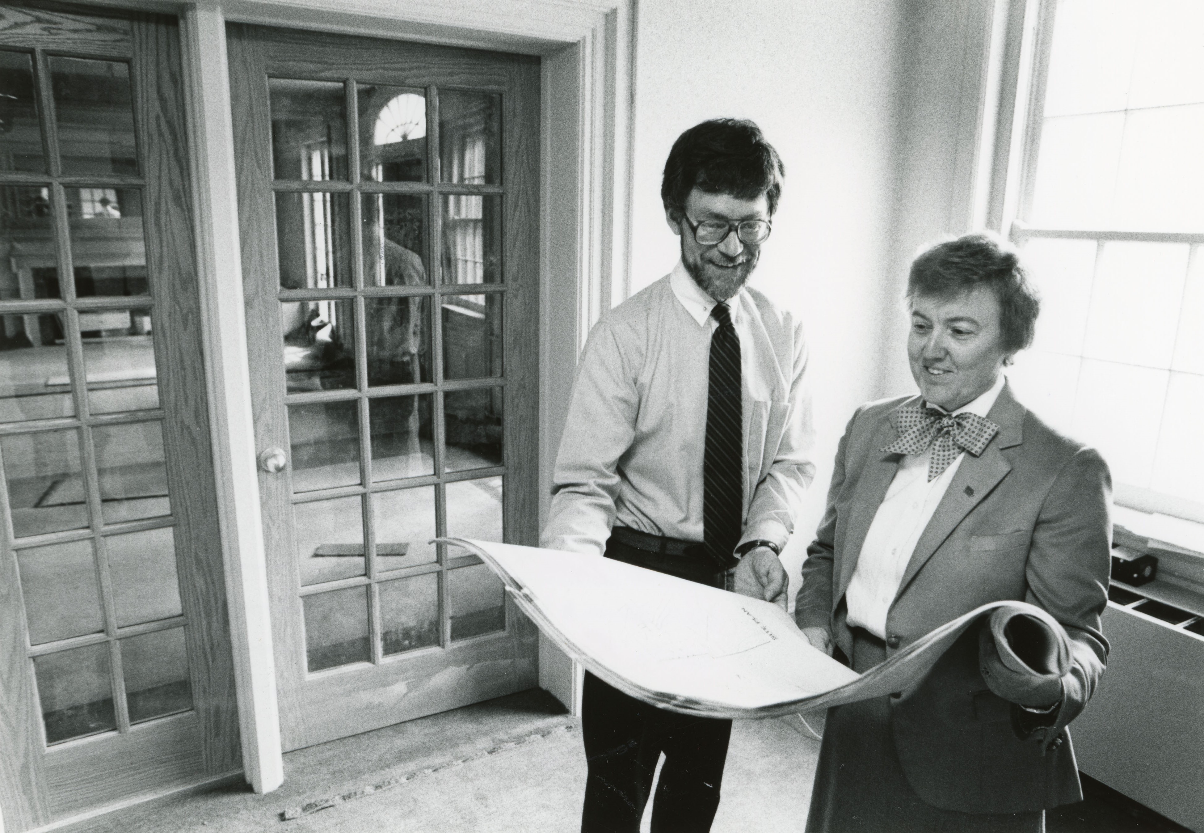 A man and woman holding and looking at a roll of building plans, doors to left showing room to be renovated