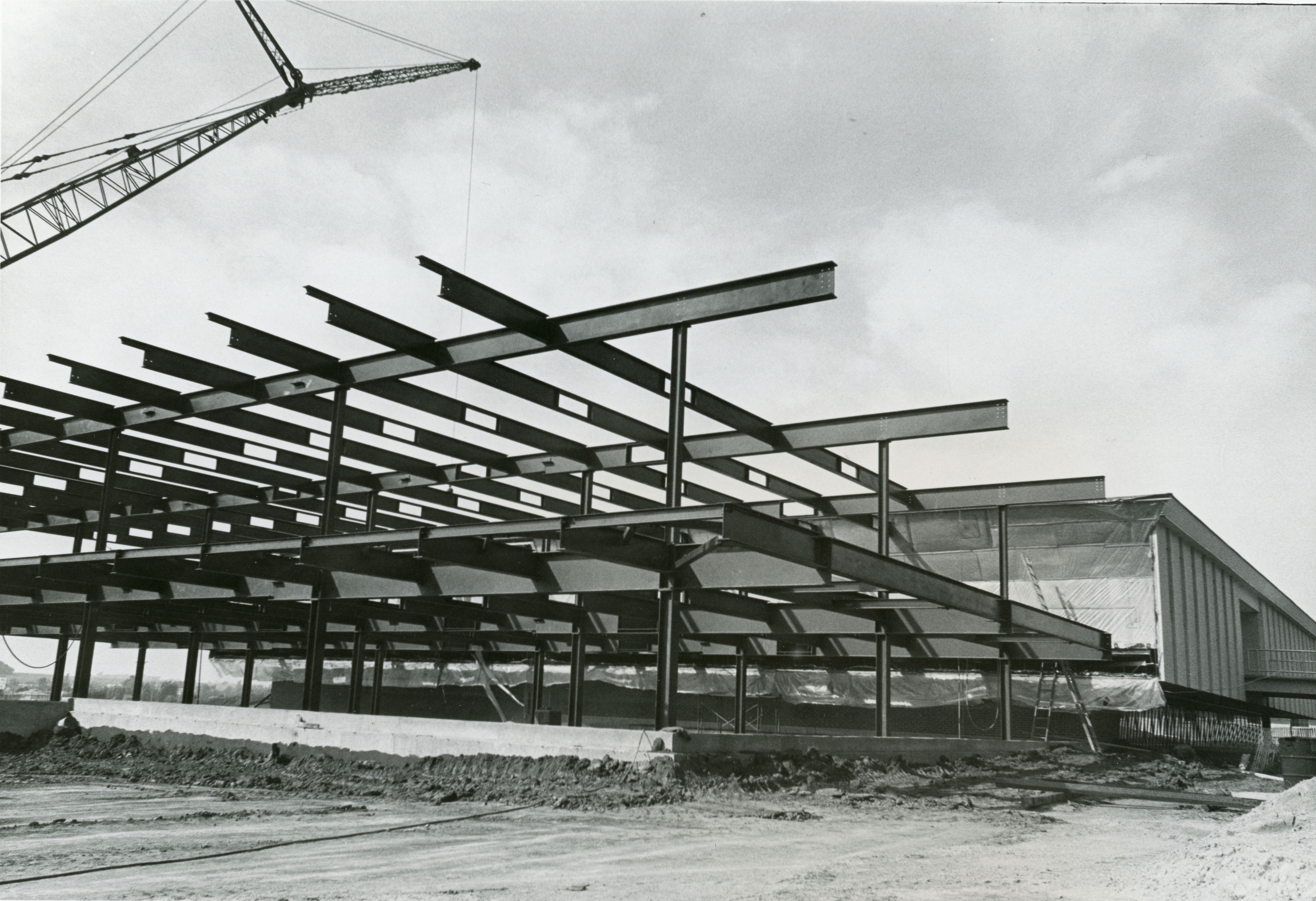 Crane lowering additional beams onto structure; completed building in background
