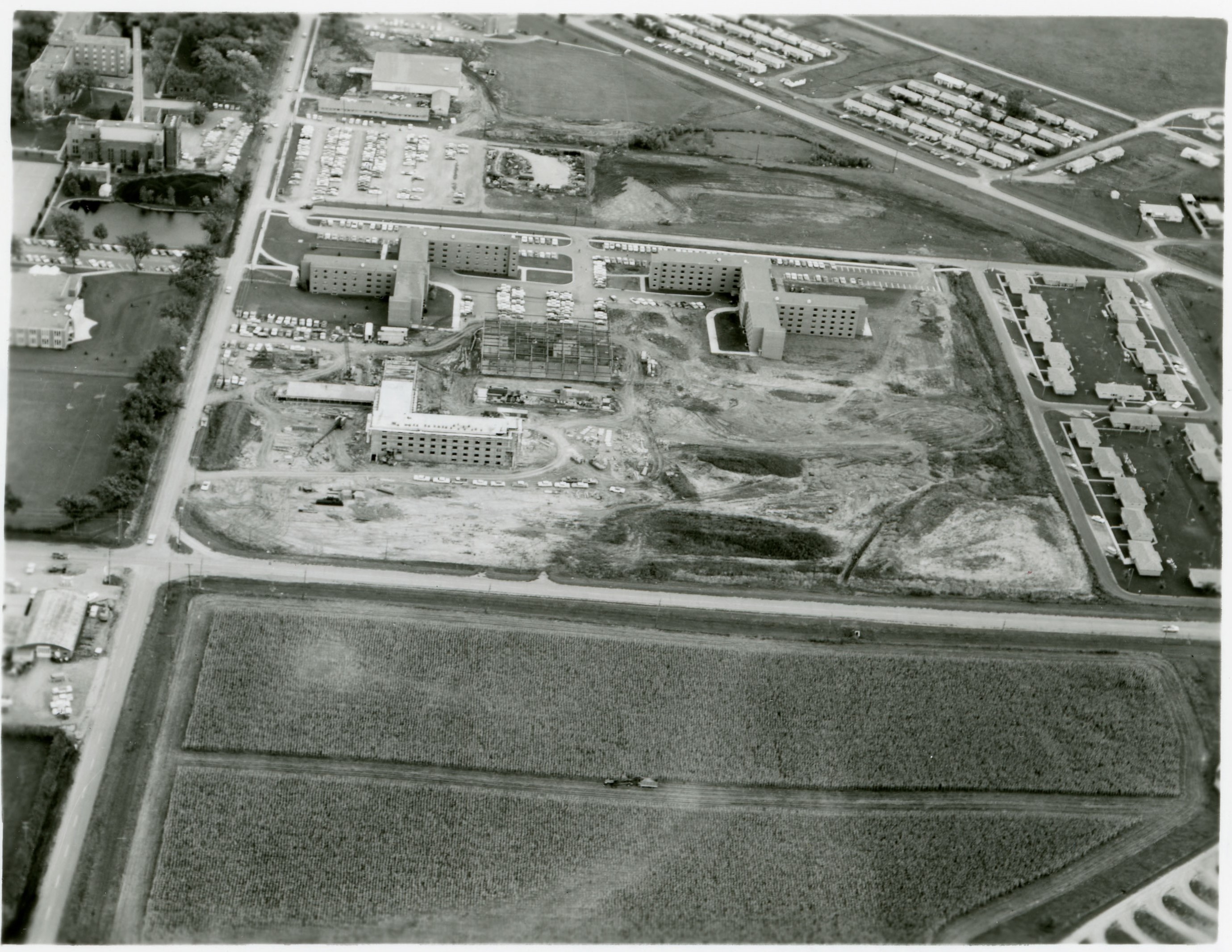 Aerial view of three completed L-shaped buildings with square building in center under construction