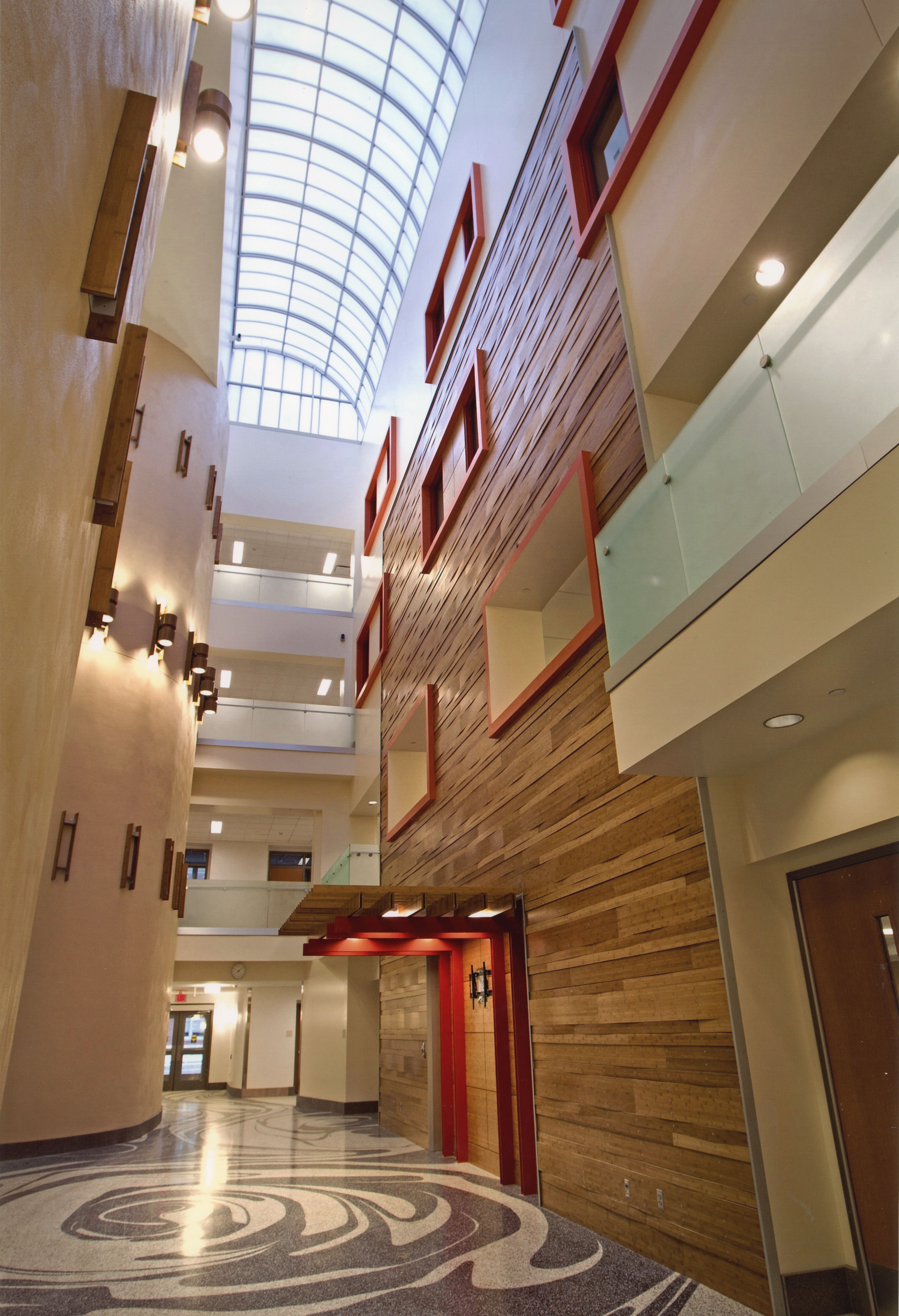 Hallway of building with glass roof, four stories of cream-colored wall to left and wood wall to right, and black and white swirled pattern on floor