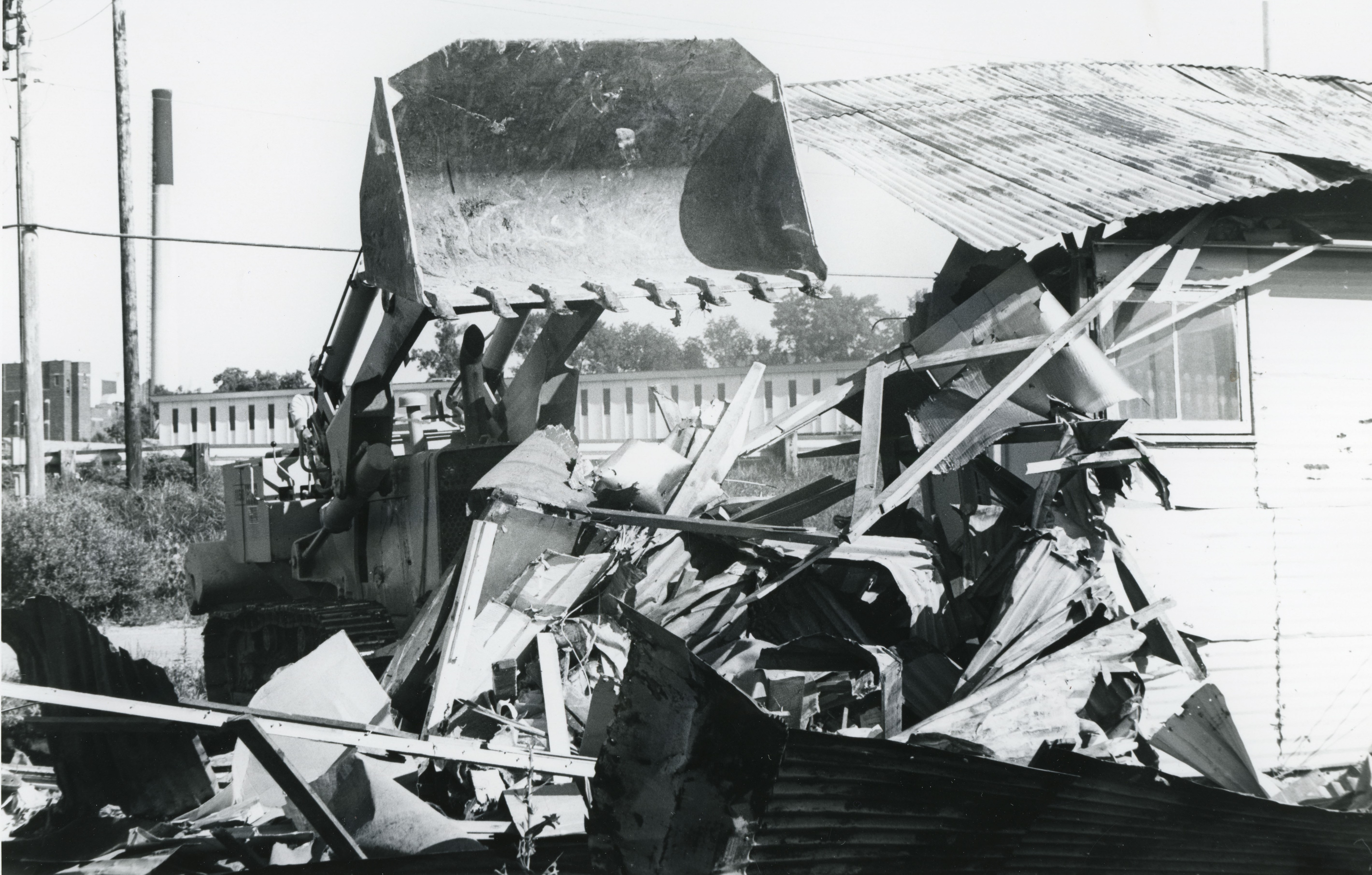 Bulldozer demolishing steel-sided building with a pile of debris in front of it and remainder of building to right
