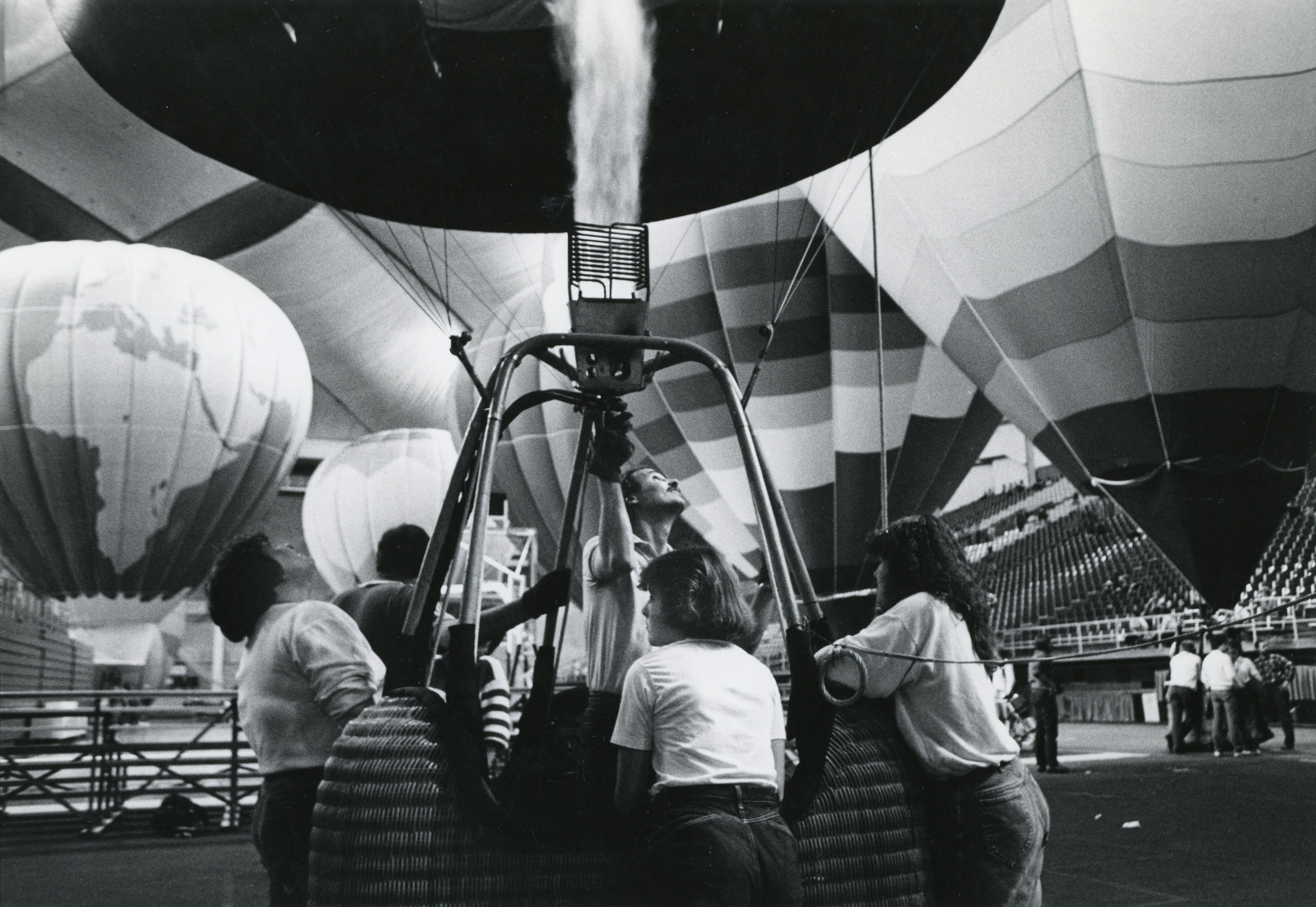 About five people around the basket of an inflated hot air balloon inside UNI-Dome with other balloons in background