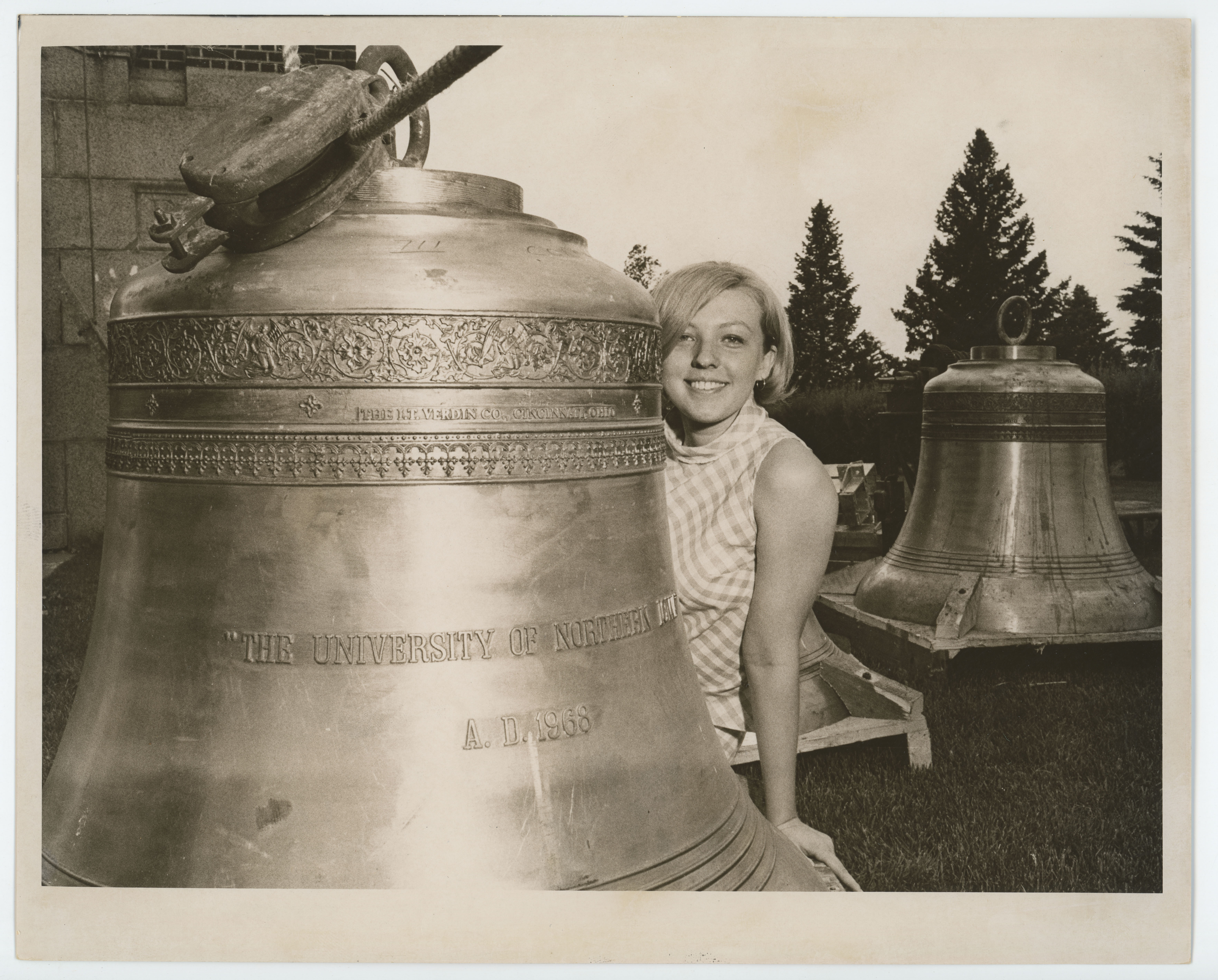 Woman leaning out from behind large bell on ground