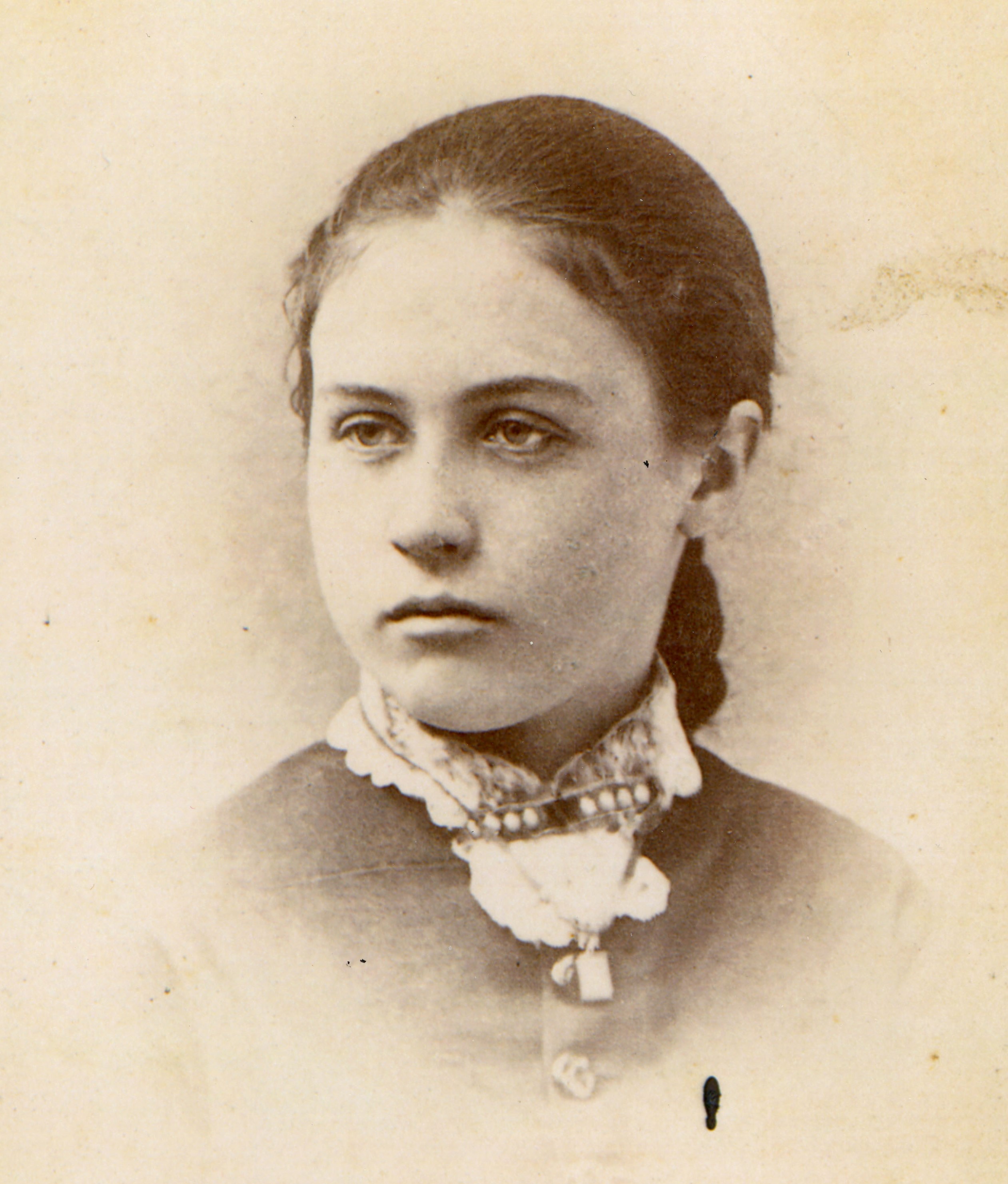 Head and shoulders view of woman with dark hair pulled back wearing a dark top with light-colored collar and jewelry