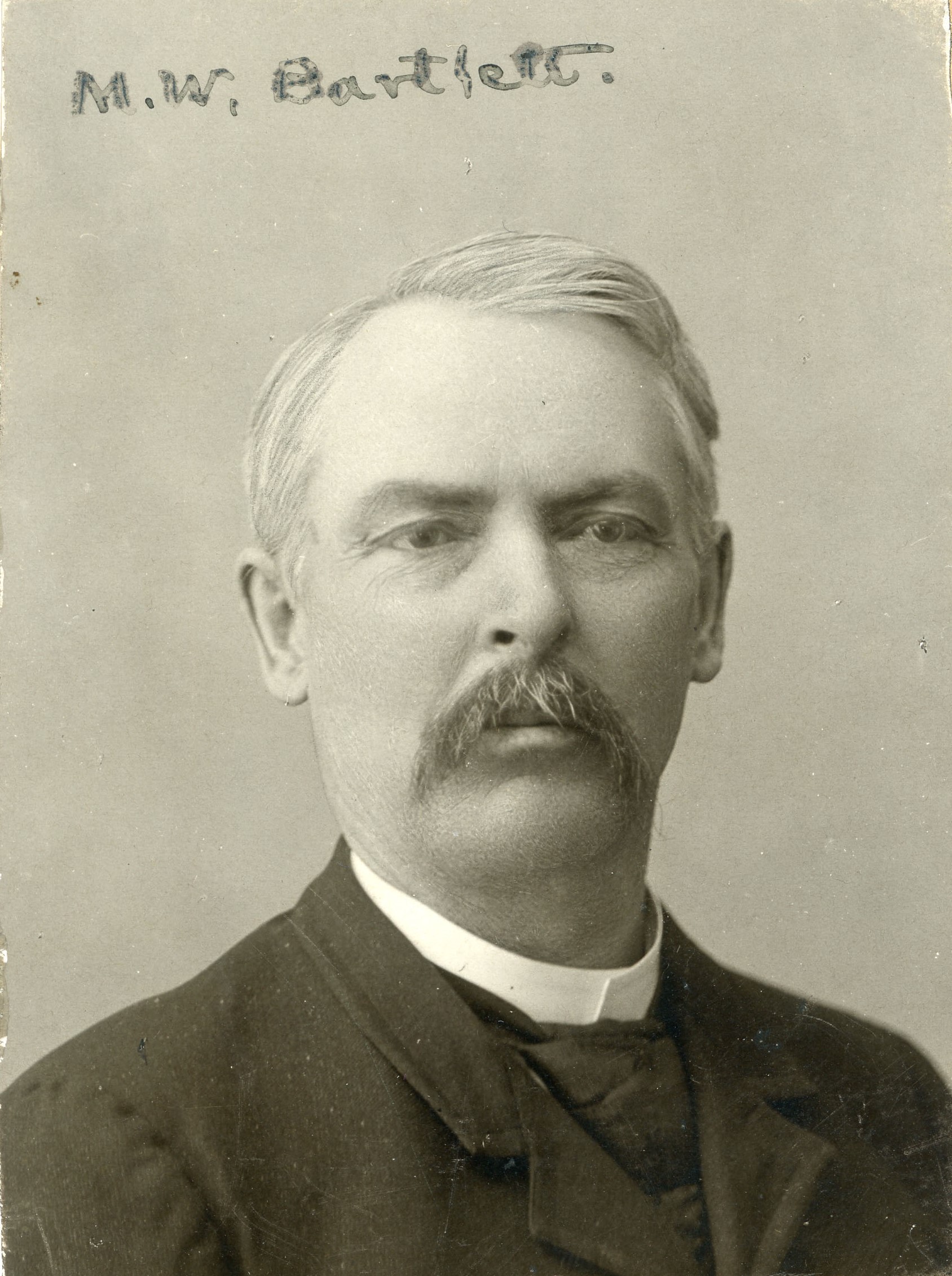 Headshot of a man with light-colored hair and slightly darker mustache wearing a dark-colored jacket and cravat with a light-colored collar; handwriting at top reads: M.W. Bartlett.