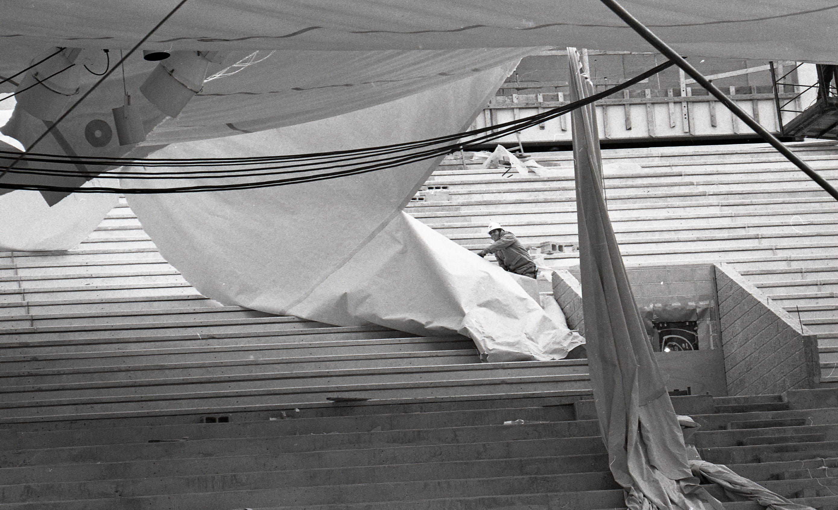 A man stands on stadium seats to pull on deflated and damaged fabric roof panel