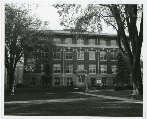 Exterior image of Begeman Hall with a bicycle in the yard and four women walking in front of the building