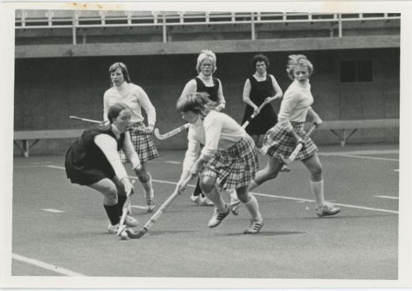 Women playing field hockey in the UNI dome, 1976