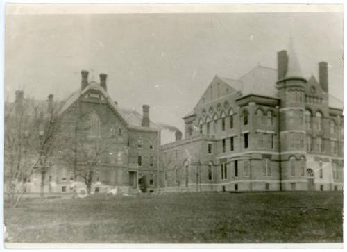 Exterior photo of the two-story corridor (center) between the Administration Building (right) and Gilchrist Hall (left). Smoke coming out of the Power Plant chimney is visible in the background