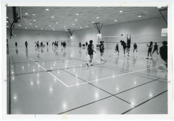 Photo of several students playing vollyball in the Physical Education Center. There are three separate groups playing at three separate nets