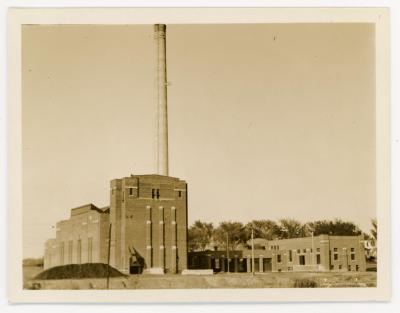 Power plant with trees in the background and a dirt hill on the left hand side. 