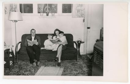 A family of four sit and read on a couch in a Sunset Village unit