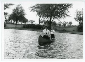 Two women wearing physical education uniforms paddle in a canoe on Prexy's Pond