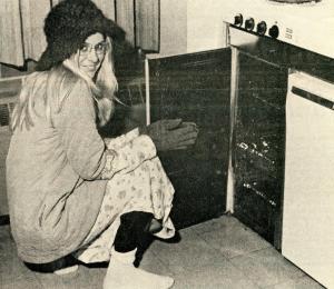 Noehren hall resident wearing warm clothes and crouching next to an oven