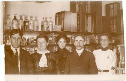 Five early chemistry students lined up in front of a shelf full of various bottles