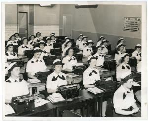 Photo of several women sitting in a typing class. All are wearing matching WAVES uniforms