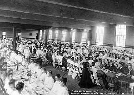 Several individuals seated at long tables in the gymnasium for an alumni banquet