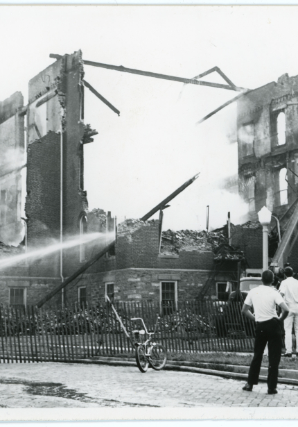 Water being sprayed on smoking ruins of brick building with people watching