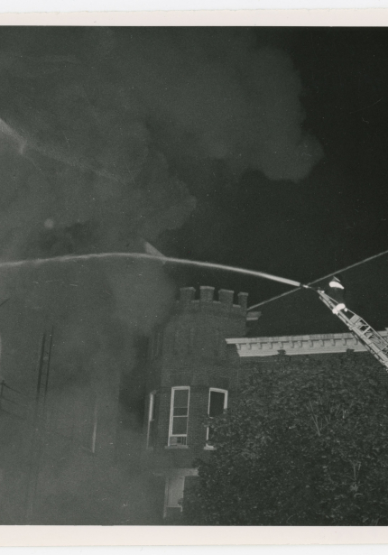 Firefighter on boom spraying hose of water at burning brick building at night