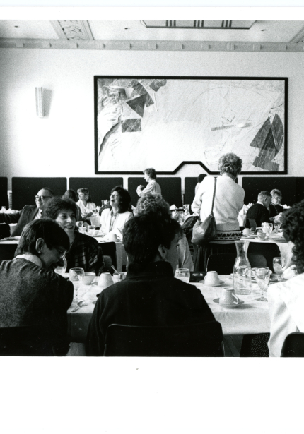 People seated at tables with refreshments in a room with abstract art on the back wall