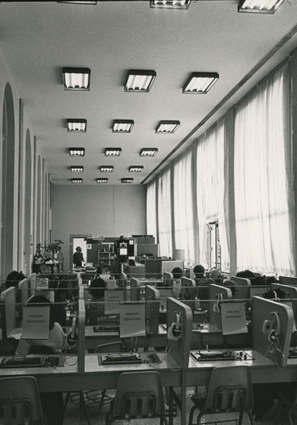 Partitioned desk tables with audio-visual equipment in closed-off terrace room with interior windows on left and exterior windows on right