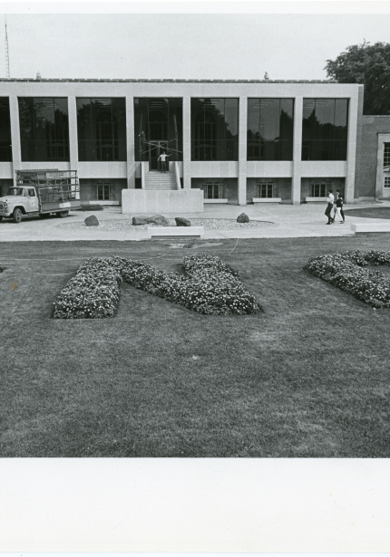 Flowerbed spelling UNI in front of Commons building, main entrance cordoned off and truck parked beside it