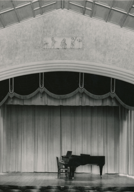 A grand piano with chair on a theatre stage in a large room