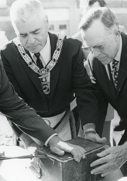 Four men gathered around a metal pox on a table, prying it open