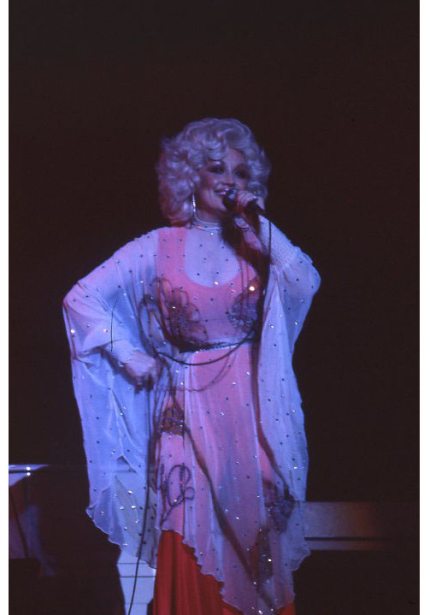 Woman in red dress with white sparkling shawl singing into microphone