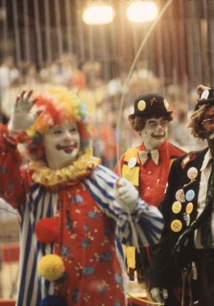 Four brightly-dressed clowns in foreground with blurred crowd in background