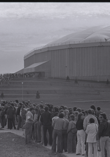 Large crowd lined up outside the UNI-Dome waiting to enter, stretching from the building down the tiered steps and to the sidewalk by the camera