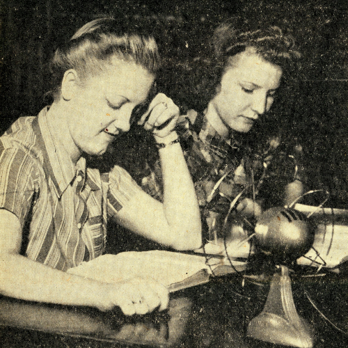 Two women studying at a table with a small metal fan in front of them