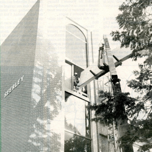 Crane lifting drywall to upper-story window and workers guiding it inside