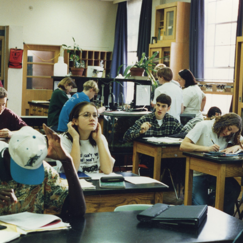 Middle or high school students at tables working with notebooks and notebooks in a science classroom with scattered potted plants