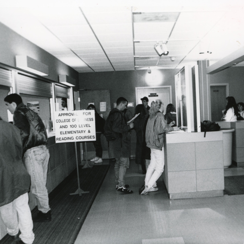 Students standing in lines and talking to people at windows, a sign reads approval for college of business and 100 level elementary & reading courses