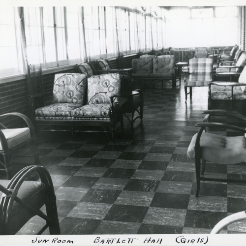 Lounge furniture in a room with a tiled floor and wall of windows to the left and back, brick to the right, caption reads: Sun Room Bartlett Hall (Girls)