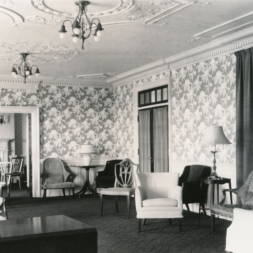 Lounge chairs and side tables scattered throughout a room with a plaster ceiling and large flower-print wallpaper