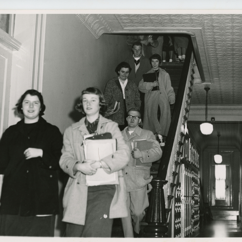 Approximately six students descending staircase to left, hallway to right