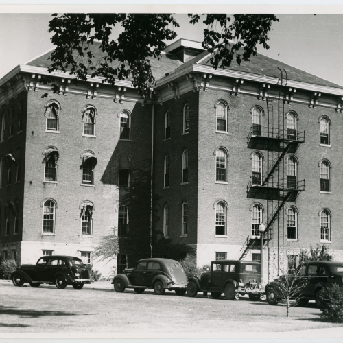 Brick building with fire escape and 1950s cars parked in front of it